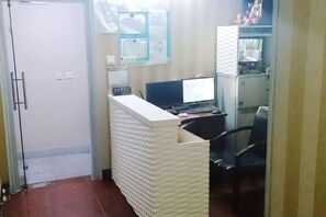 Un mostrador de recepción con una computadora, una silla y una mampara de vidrio.