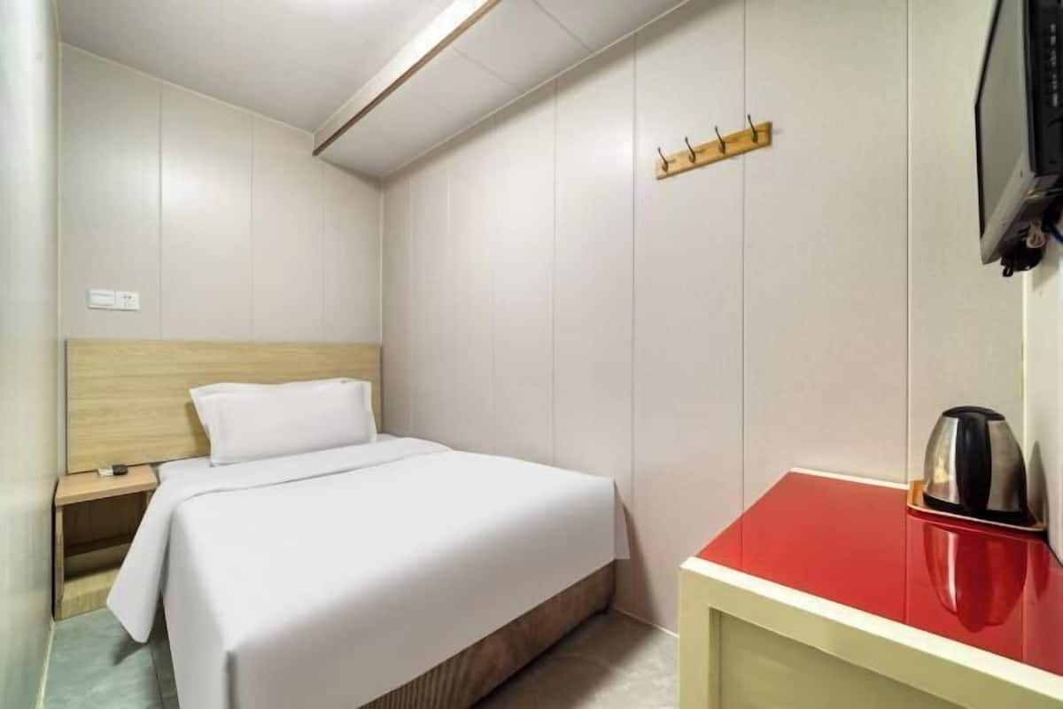 A hotel room with a bed, a nightstand, a red and white cabinet, and a wall-mounted television.