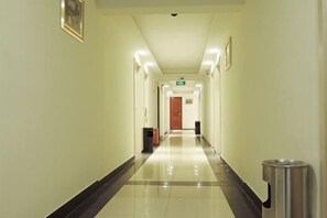 A hotel hallway with a polished floor, a trash bin, and a door at the end.