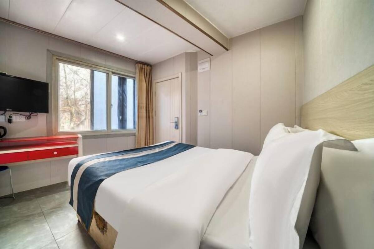 A hotel room with a bed, a desk, a TV, and a window with curtains.