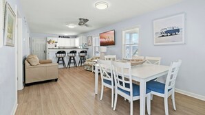 Un espacio habitable compacto con kitchenette, una zona de comedor con mesa y sillas blancas, y un sofá en la sala.