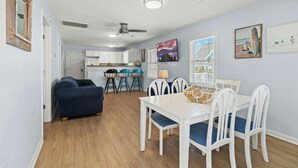 Una cocina moderna con armarios blancos, un comedor con mesa blanca y sillas azules, y un ventilador de techo.