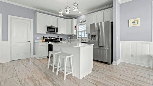 A modern kitchen with white cabinetry, a stainless steel refrigerator, and a central island with bar stools.