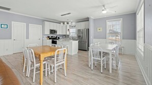A modern kitchen with white cabinets, stainless steel appliances, and a dining area with a wooden table and white chairs.