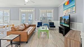 A living room with a leather sofa, two blue chairs, a green coffee table, a TV on a stand, and a painting of a beach scene.