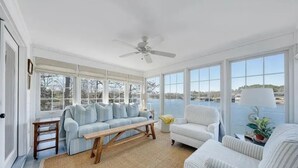 A sunroom with a large window overlooking a body of water, a ceiling fan, and a seating area with a bench and two chairs. - Lakefront Property! Gentle slope to the water, firepit, water skis, paddleboards (Moneta)