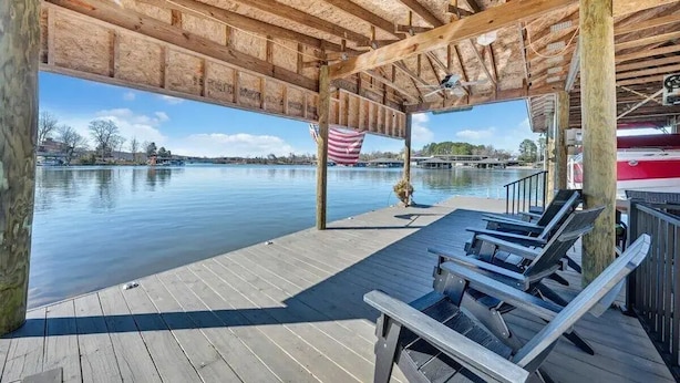 A wooden deck with lounge chairs overlooking a calm lake, an American flag, and a covered area with a view of the water. - Lakefront Property! Gentle slope to the water, firepit, water skis, paddleboards (Moneta)