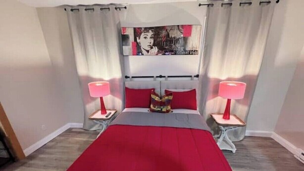 A bedroom with a bed, two bedside tables with lamps, a red bedspread, and a poster on the wall.