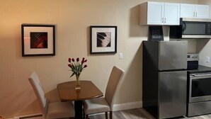 A small kitchen with a refrigerator, microwave, and oven. There are framed pictures on the wall and a vase with flowers on a table.