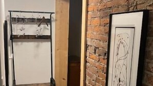 A narrow hallway with a wooden bunk bed, a brick wall, and a framed abstract painting.