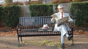A bench with a plaque, a hat, and a book.