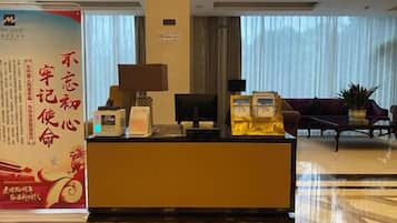 Uma área de recepção de hotel com balcão, televisão e um espaço de estar com sofá e mesa de centro.