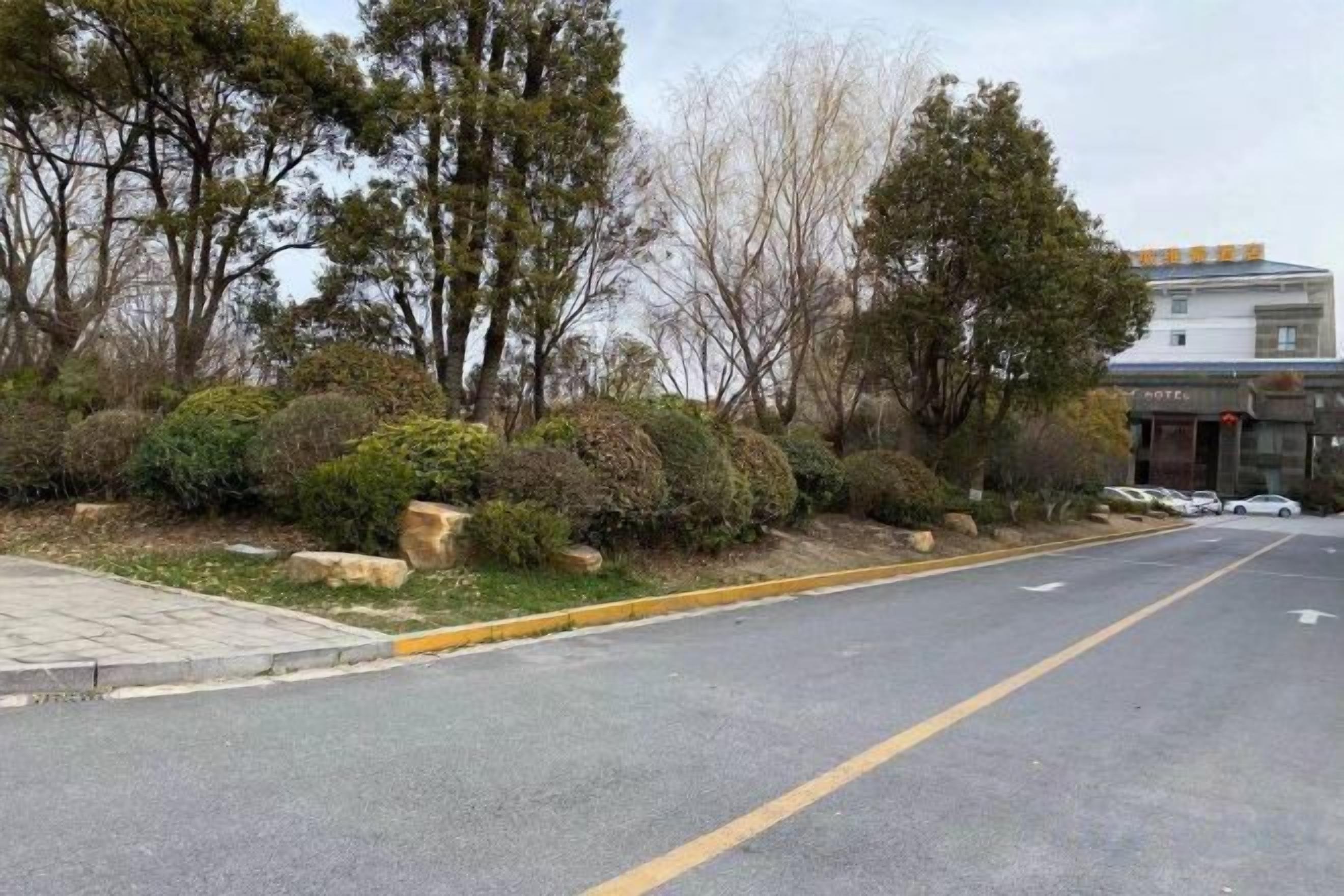 A street with a sidewalk, trees, and a building with a sign.