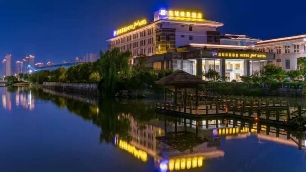 A hotel with a reflection in the water, featuring a modern design and a well-lit facade. - Metropark Hotel Yancheng (Yancheng)
