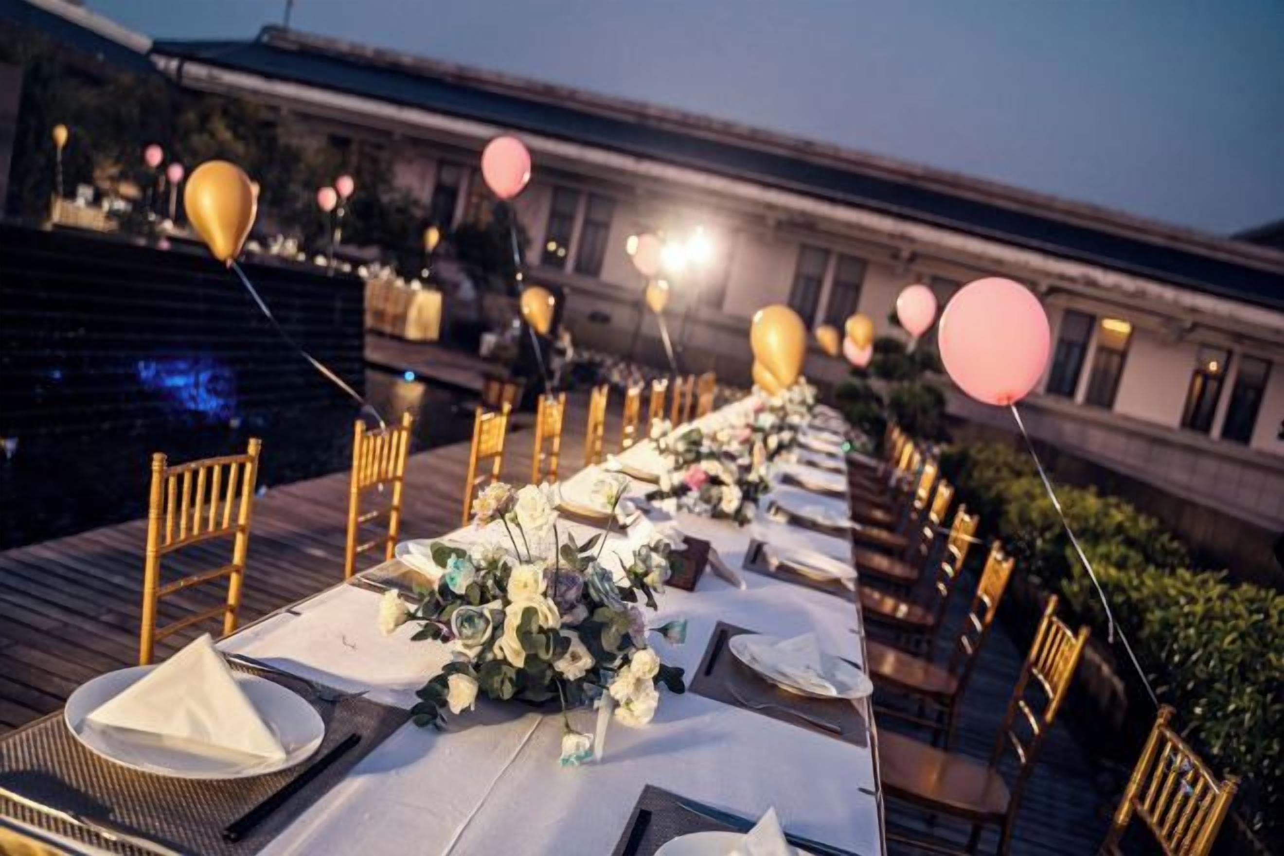Un área de comedor al aire libre con mesas dispuestas para una comida, sillas y globos.