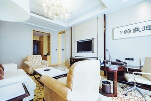 Habitación de hotel con sofá, sillones, televisión, escritorio y candelabro.