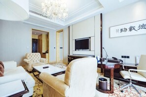 Habitación de hotel con sofá, sillones, una mesa de centro, televisión, escritorio y candelabro.