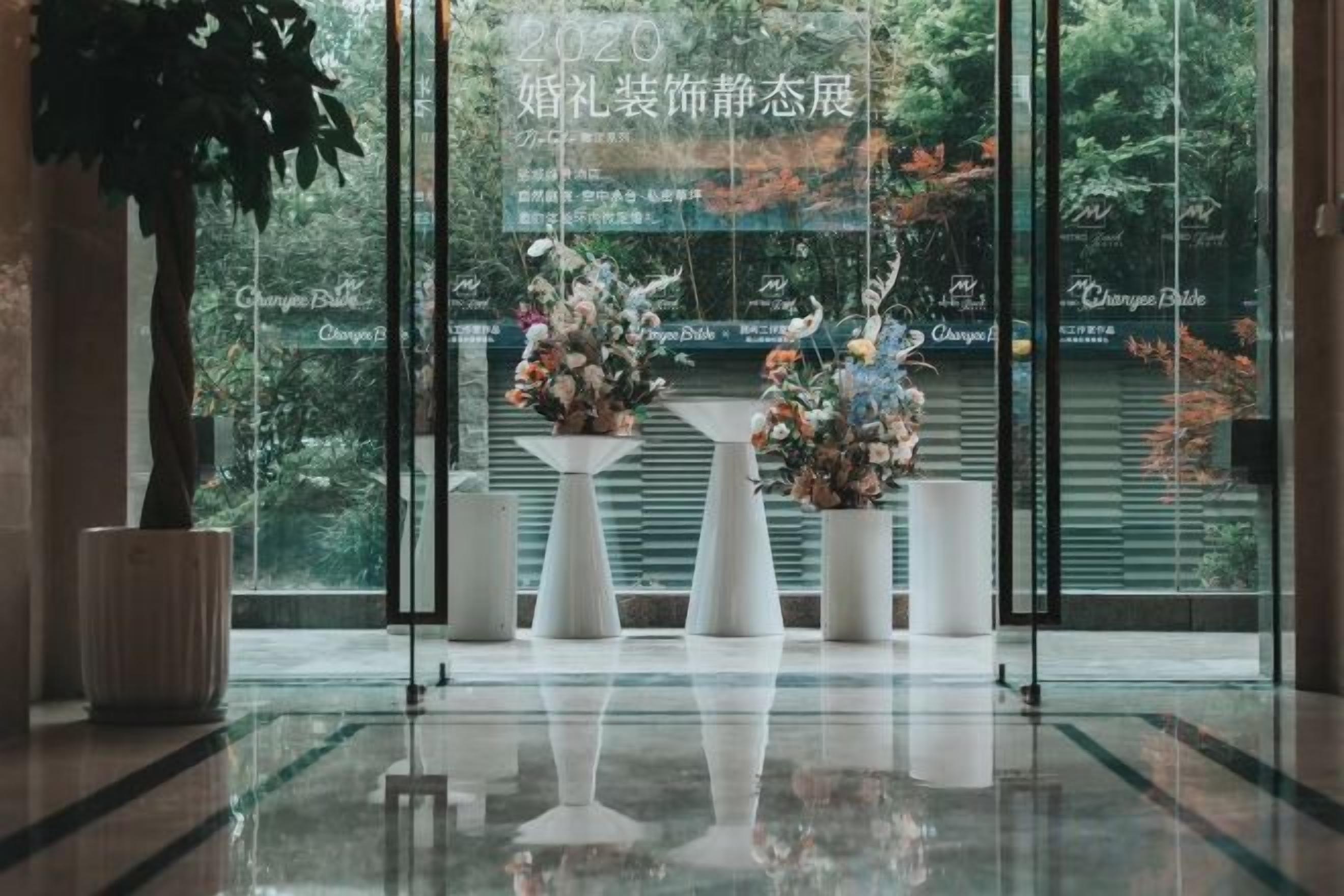 Un área de recepción con un muro de vidrio, plantas en macetas y arreglos florales.