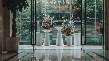 Un área de recepción con un muro de vidrio, plantas en macetas y arreglos florales.