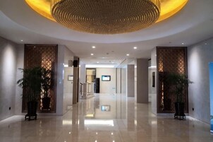 Un moderno vestíbulo de hotel con piso pulido, una gran lámpara circular y plantas en macetas.