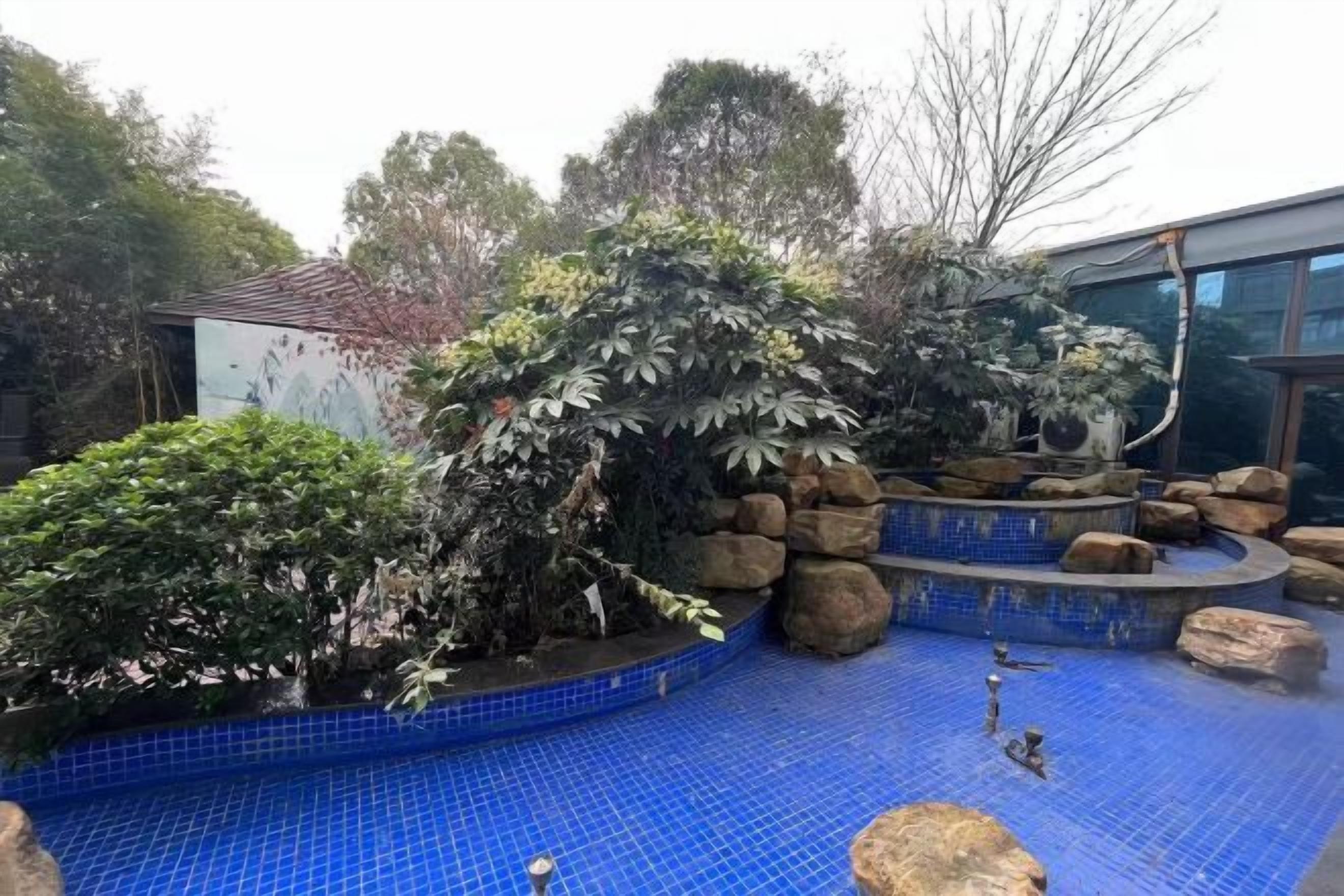 Una piscina con baldosas azules, rodeada de rocas y plantas.