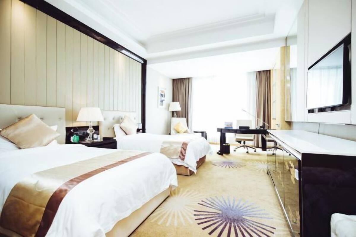 A hotel room with two beds, a desk, a TV, and a large window.