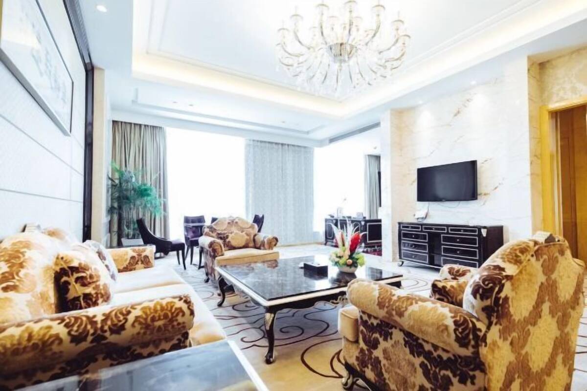 A spacious living room with a chandelier, a flat-screen TV, and patterned sofas.