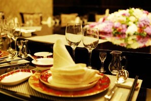 A dining table set with plates, glasses, and cutlery, with a vase of flowers in the background. - Metropark Hotel Yancheng (Yancheng)