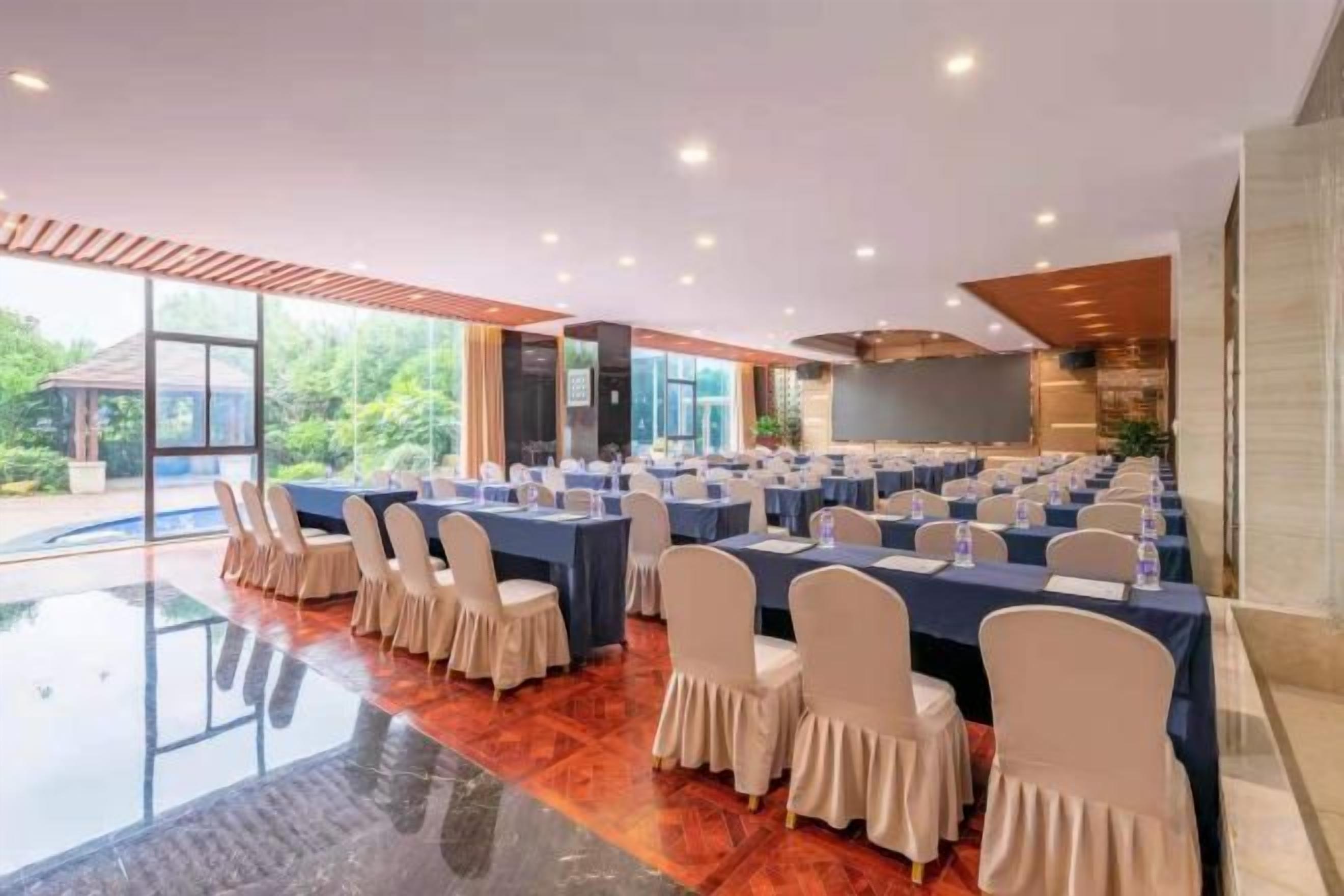 A conference room with multiple tables and chairs, large windows, and a view of greenery outside.