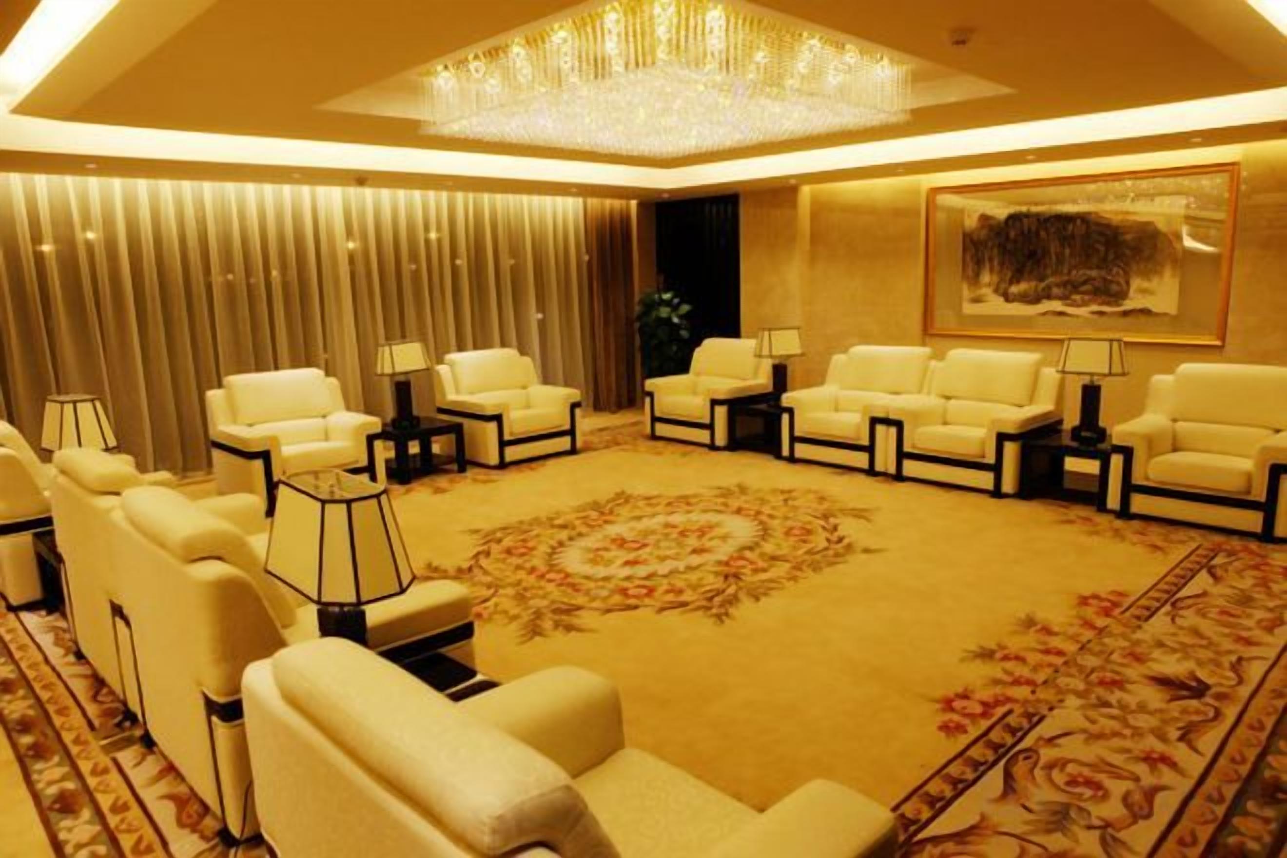 Um lounge de hotel com diversas áreas de estar, um candelabro e um tapete grande.