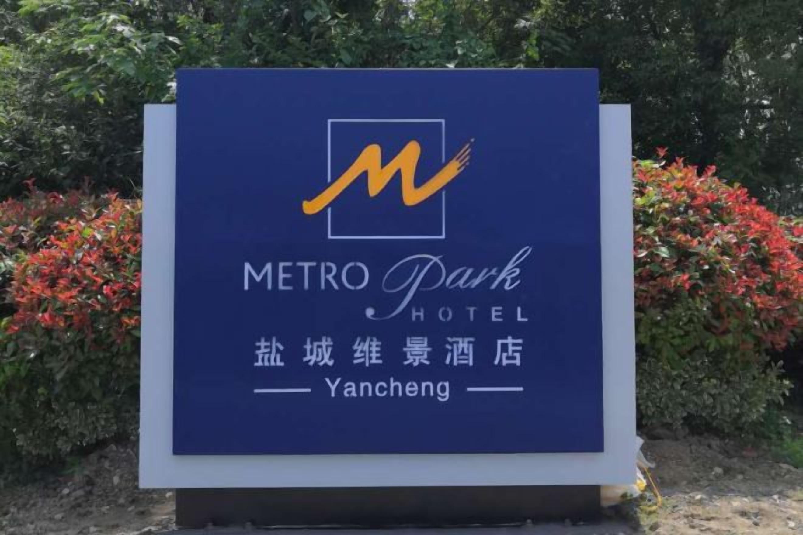 Un letrero para el Metro Park Hotel con un logotipo estilizado 'M', nombre en inglés y chino, y un nombre de ubicación.