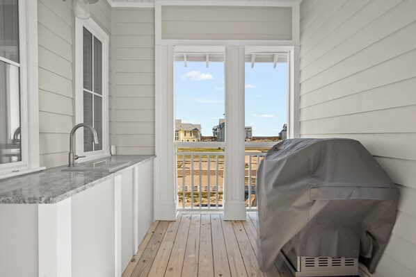 A balcony with a grill, a window, and a view of buildings. - Coastal Breeze 126 SEA (Port Aransas)