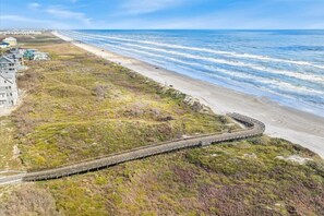 En kustväg med en bro som svänger över en strand och leder till ett bostadsområde med hus.