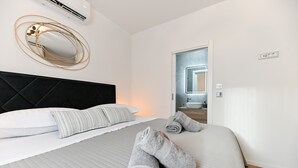Een opgemaakt bed met wit en grijs beddengoed, een zwart hoofdbord en twee handdoeken gerold op het bed.