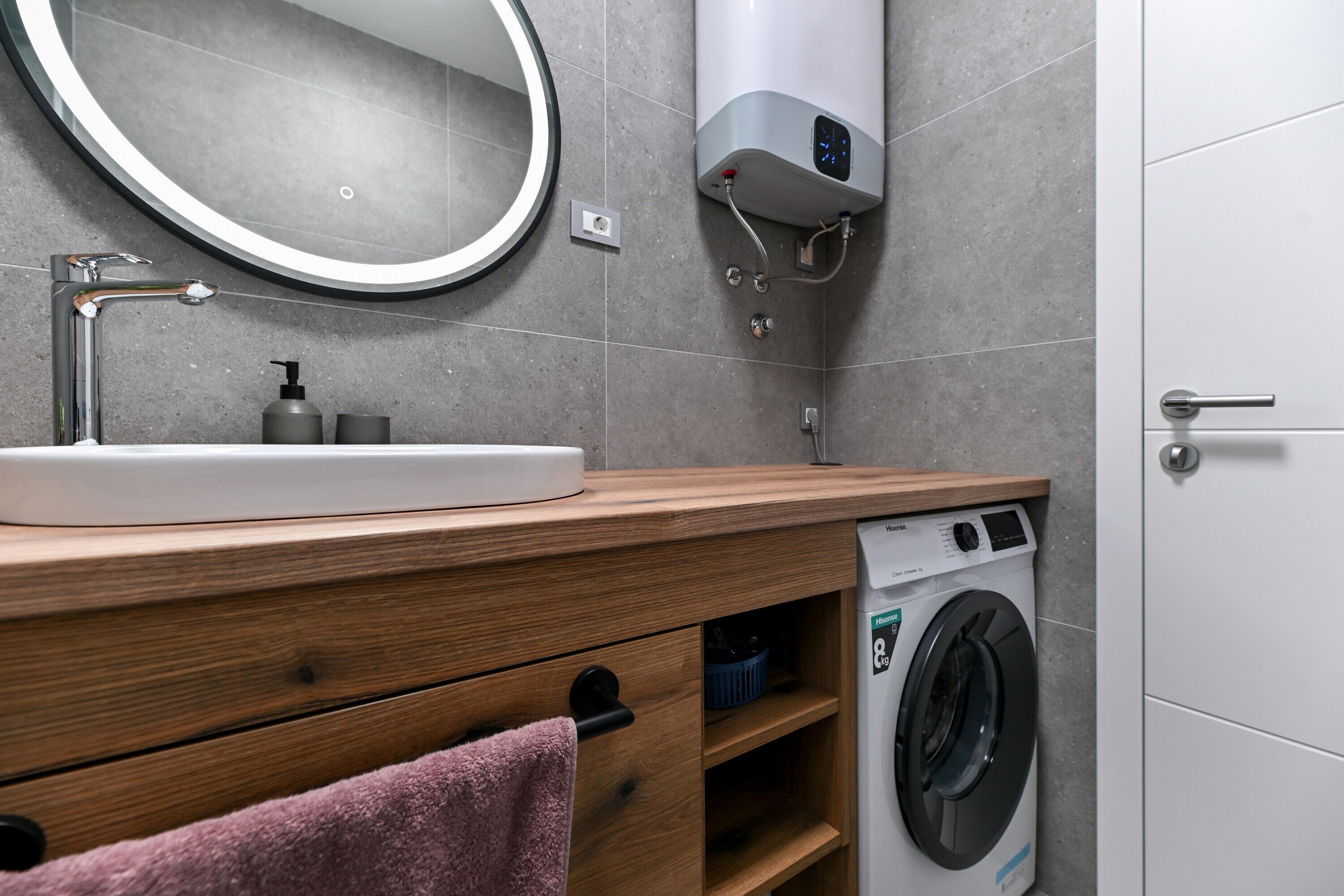 A modern bathroom with a wooden vanity, a sink, a mirror, a towel, a washing machine, and a towel rack.