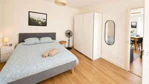 Ein Schlafzimmer mit Bett, Nachttisch, Lampe, Ventilator, Kleiderschrank, Spiegel und einem gerahmten Bild an der Wand.