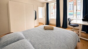 Een slaapkamer met een bed, bureau, stoel, kledingkast en een raam met gordijnen.