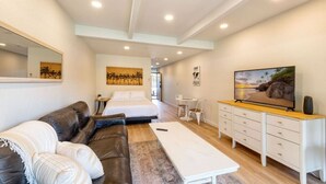 A modern hotel room with a bed, a sofa, a small table, a TV, and a cabinet. - Walk to Beach! Pool, Hot Tub + AC Studio (Kihei)