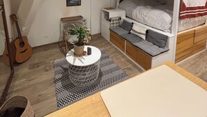 Une chambre de type dortoir avec un lit superposé, une guitare, une petite table avec une plante et une affiche accrochée au mur.