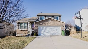A two-story house with a garage, a basketball hoop, and a clear driveway. - Spacious 4 bedroom house with AC, WiFi in, 2 living rooms, fenced, 2 car garage. (Omaha)