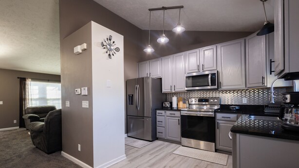 A modern kitchen with stainless steel appliances, grey cabinets, and a dining area with a dark countertop. - Spacious 4 bedroom house with AC, WiFi in, 2 living rooms, fenced, 2 car garage. (Omaha)