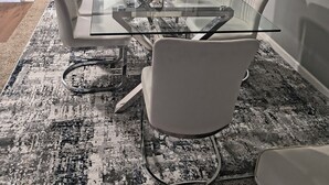 A dining area with a glass table, white chairs, and a patterned rug. - Spacious 4 bedroom house with AC, WiFi in, 2 living rooms, fenced, 2 car garage. (Omaha)