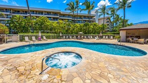 Une piscine d’hôtel avec un jacuzzi, entourée de palmiers et de chaises longues.