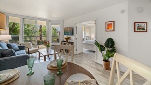 Una sala moderna con sofá, mesa de comedor y sillas, un área de cocina con mesa, y un dormitorio con cama, y un baño visible a través de un umbral abierto.