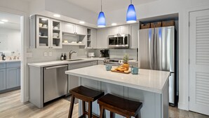 Una cocina moderna con armarios grises, electrodomésticos de acero inoxidable y una isla central con taburetes.