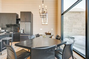 A modern kitchen with dark cabinetry, a stainless steel refrigerator, and a dining area with a large table and chairs. - Modern Ski-In/Out Home in Brian Head w/ Deck (Brian Head)