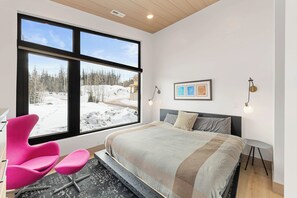 A bedroom with a large window, a bed, a chair, and a bedside table. - Modern Ski-In/Out Home in Brian Head w/ Deck (Brian Head)