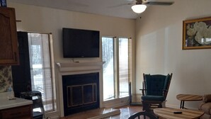 A living room with a fireplace, a television mounted above it, and a dining area with a table and chairs. - Percy Quinn Vacation Rental A (McComb)