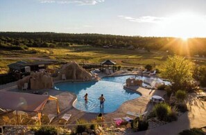 Un área de piscina con varias piscinas, sillas de descanso y un pabellón.