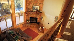 A cozy living room with a fireplace, wooden furniture, and large windows offering a view of trees. - Zion Views-Sunset Cabin+Resort Access (Orderville)